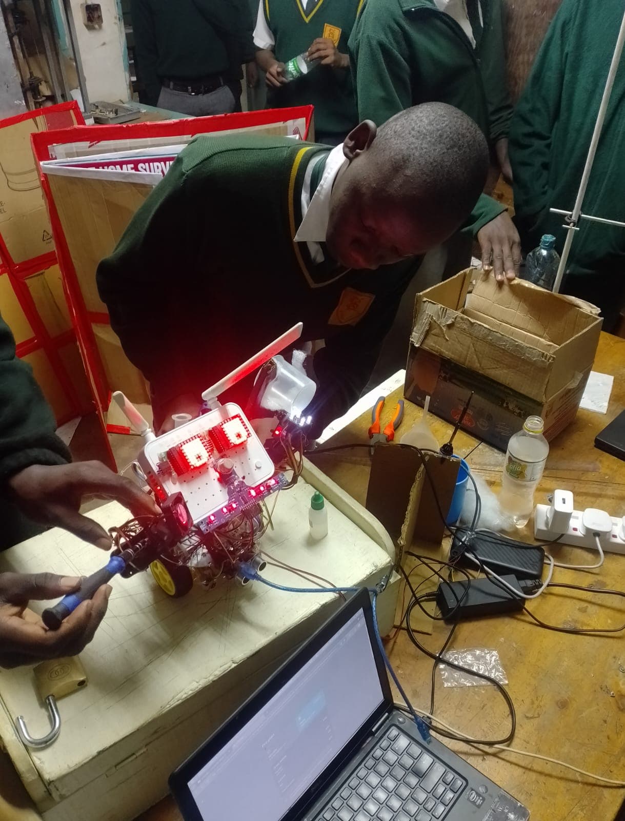 Students and mentor testing autonomous mobile robot on workshop table